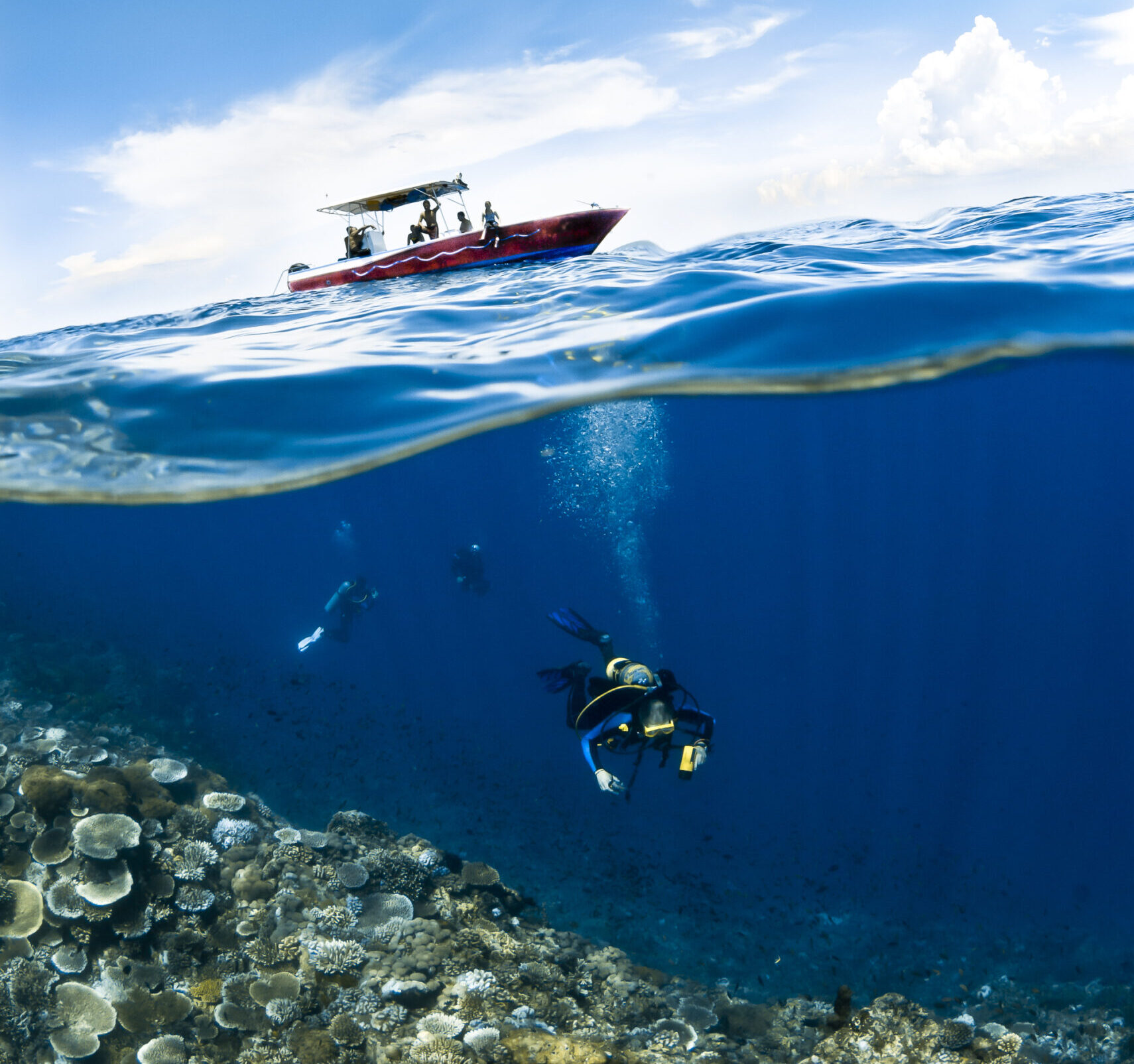 Scuba diver underneath small red motor boat investigating coral.