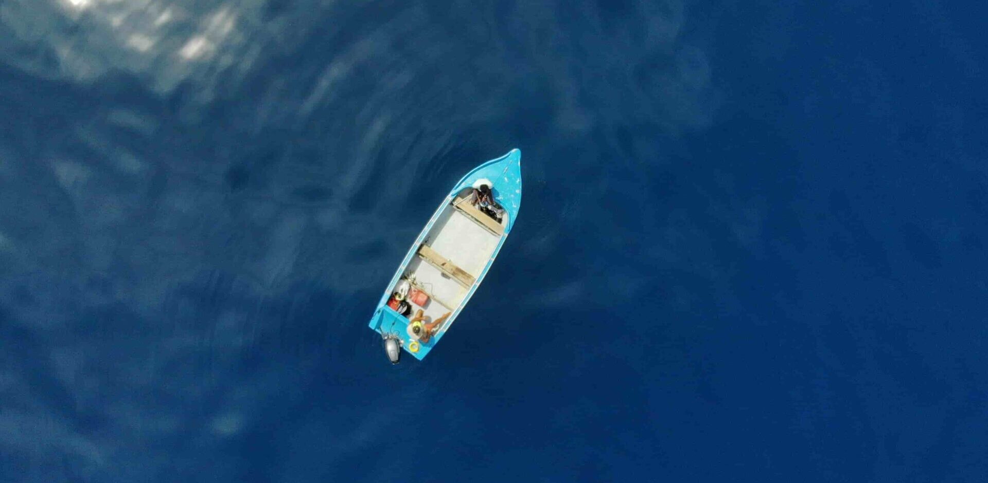Areal photo of a blue fishing boat in the open ocean.