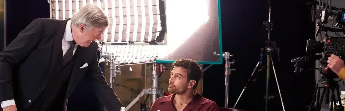 Stephen Fry serving a plate to Theo James seated at a table